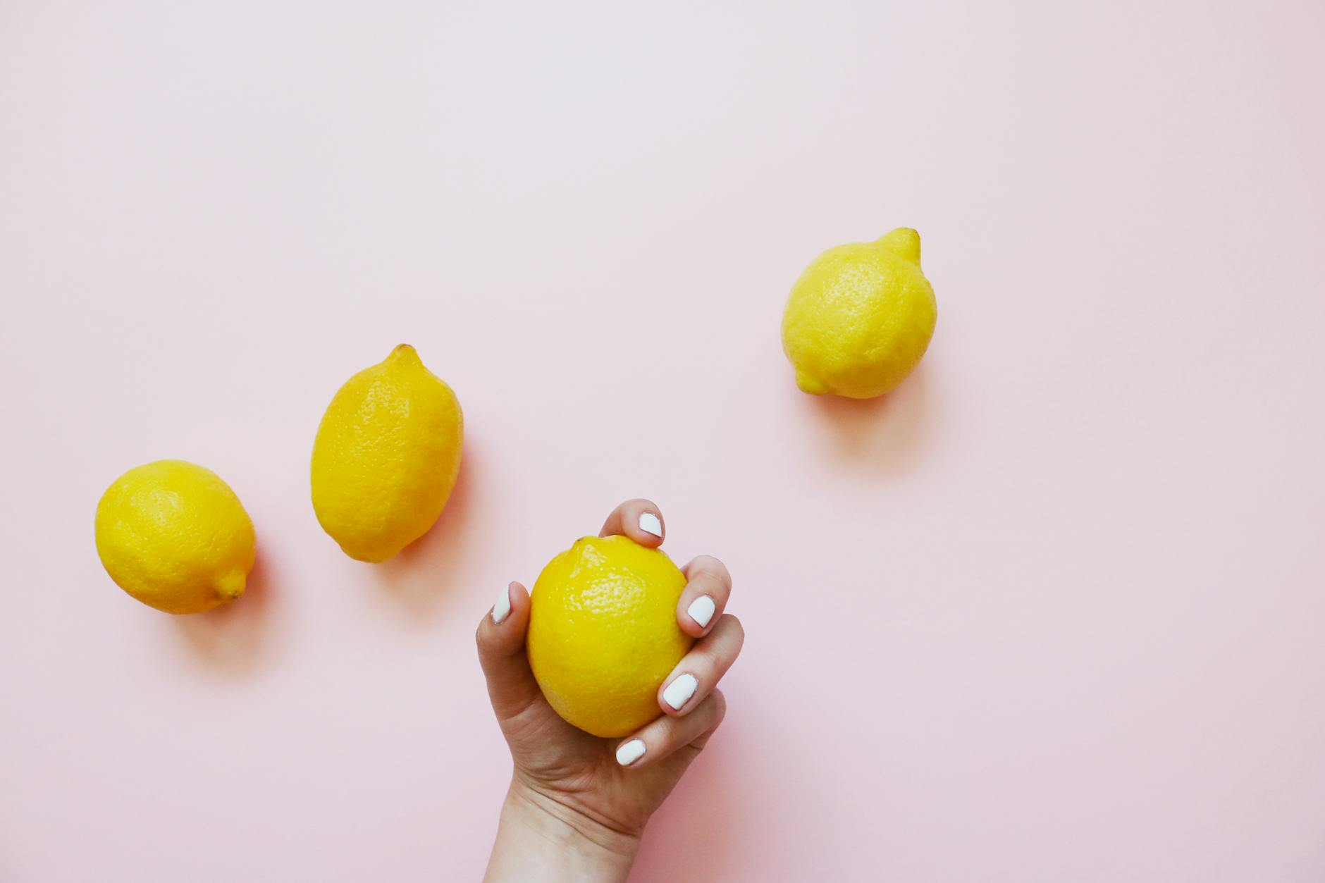 A hand holding a fresh lemon on soft pink background, symbolizing the simplicity and directness of a lemon vibrator solution