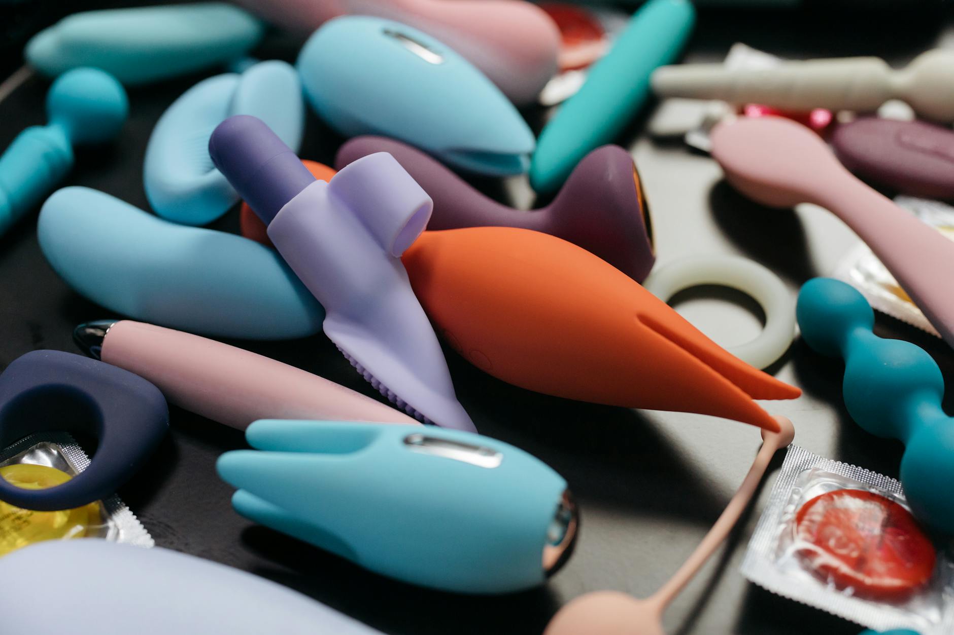 Two hands holding pink and blue silicone vibrators against a pastel background, representing accessibility and choice in sexual wellness tools.