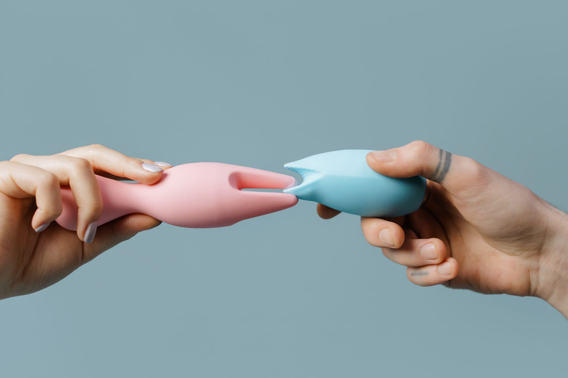 Hands holding colorful silicone vibrators against a purple background