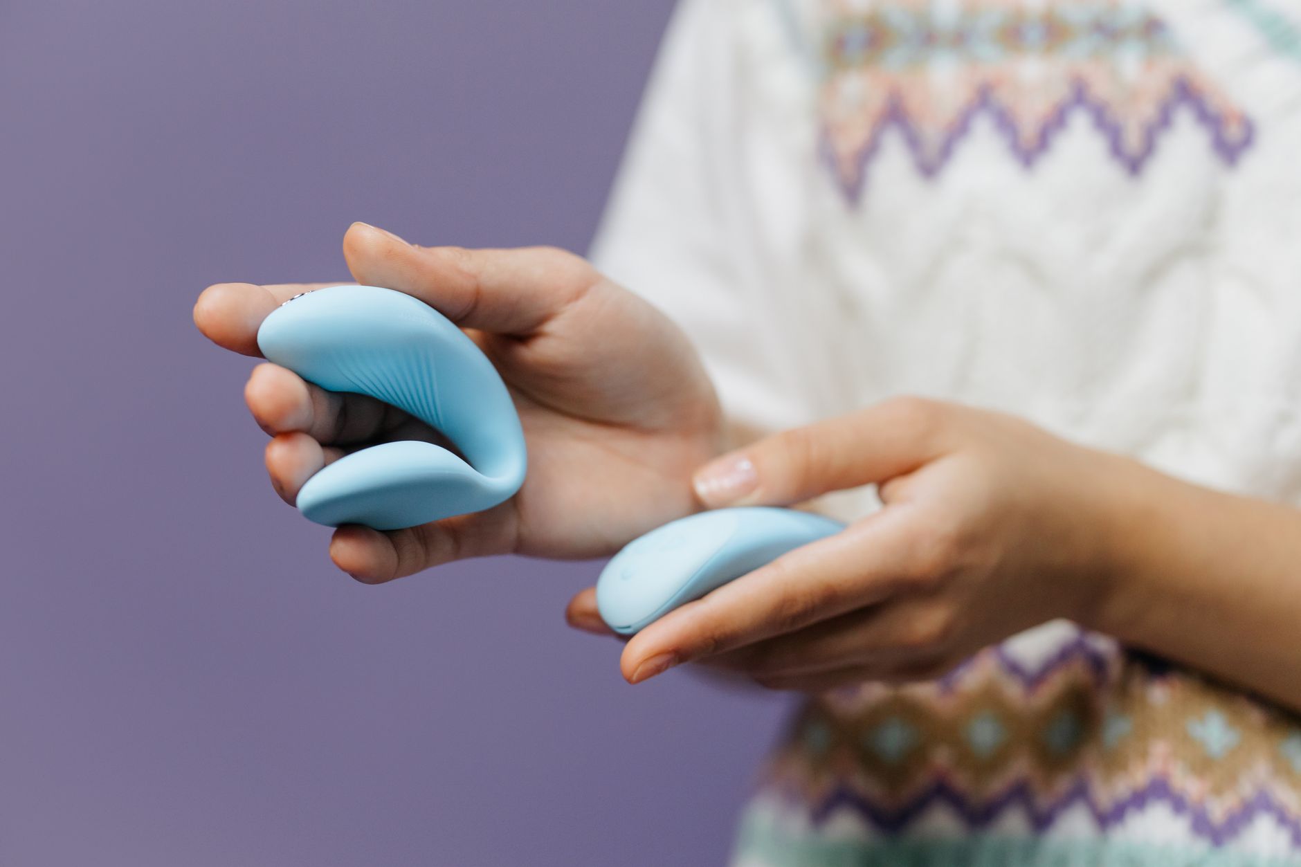 Close-up of hands holding a sleek blue vibrator against a purple background, demonstrating controlled grip and intensity.