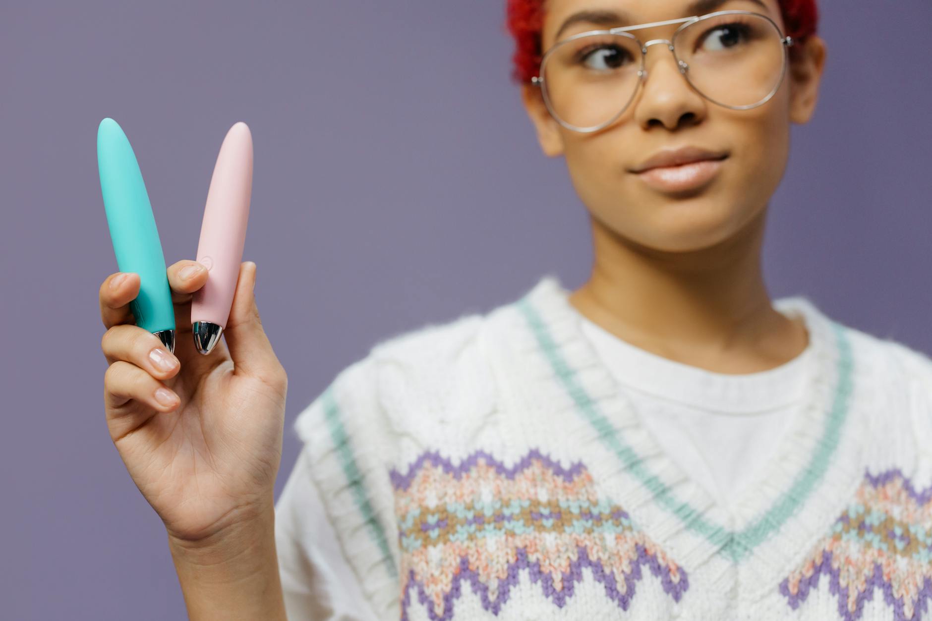 A person holding colorful vibrators against a purple background, representing self-pleasure and body ownership.