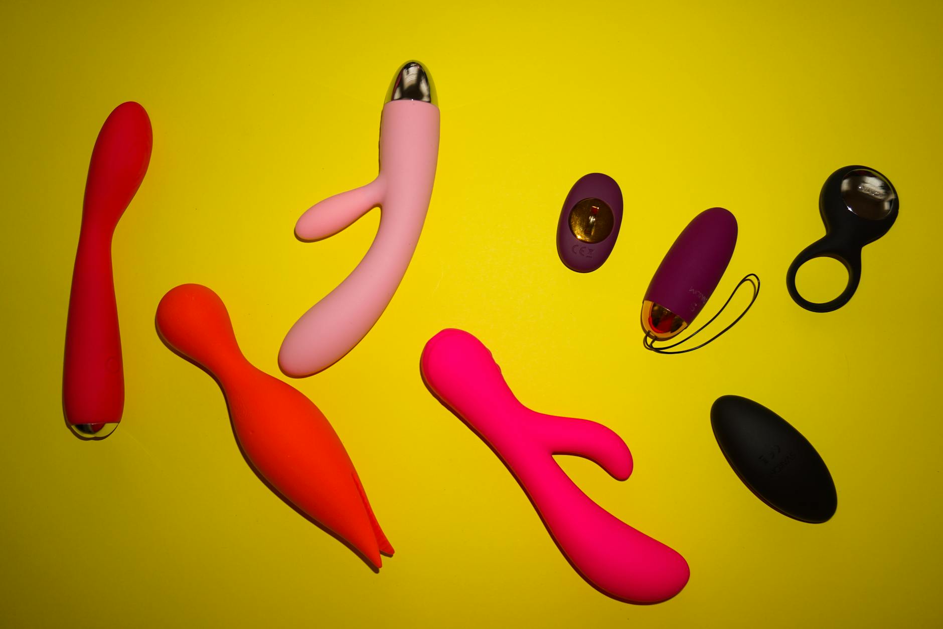 Vibrant collection of colorful clitoral vibrators and sex toys on a bright yellow background